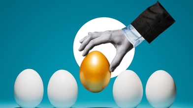 The hand chooses the golden egg among the white eggs.