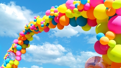 Colourful balloon arch against blue cloudy sky